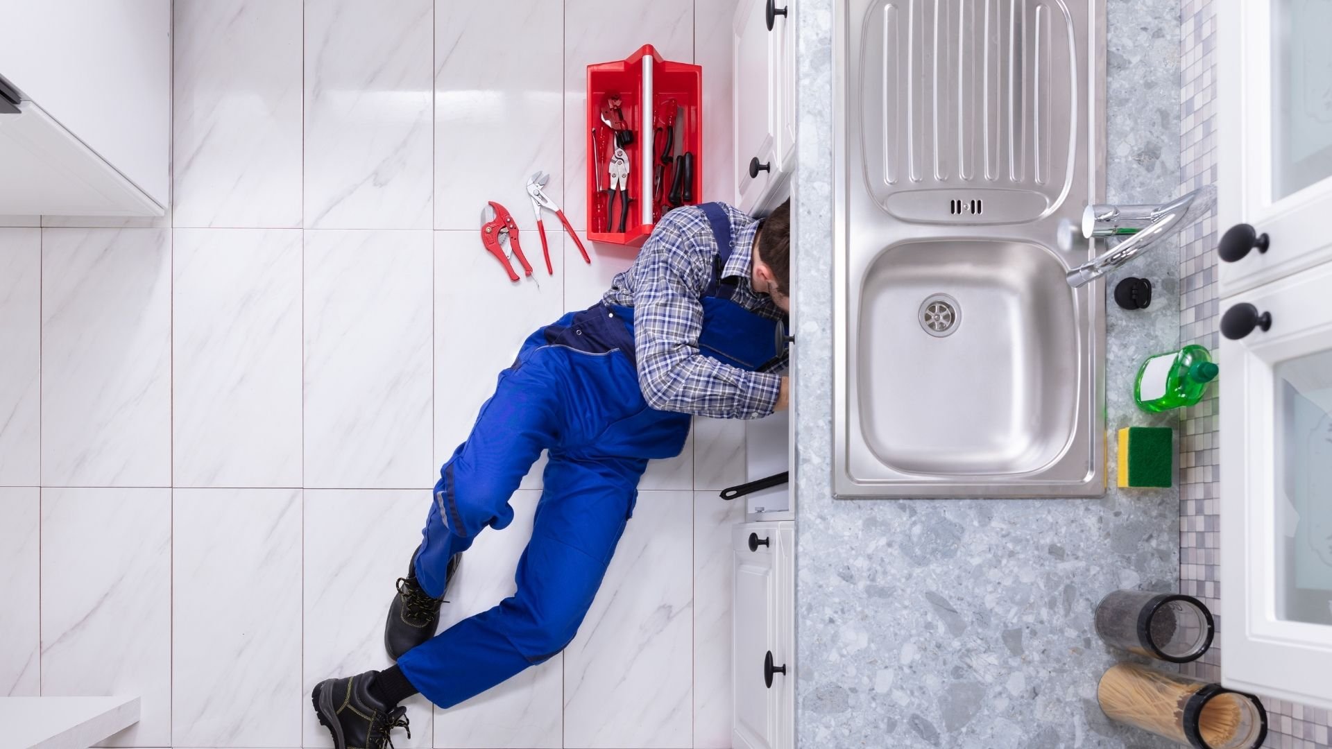 Plumber fixing pipes under a kitchen sink with a toolbox in North Hollywood CA