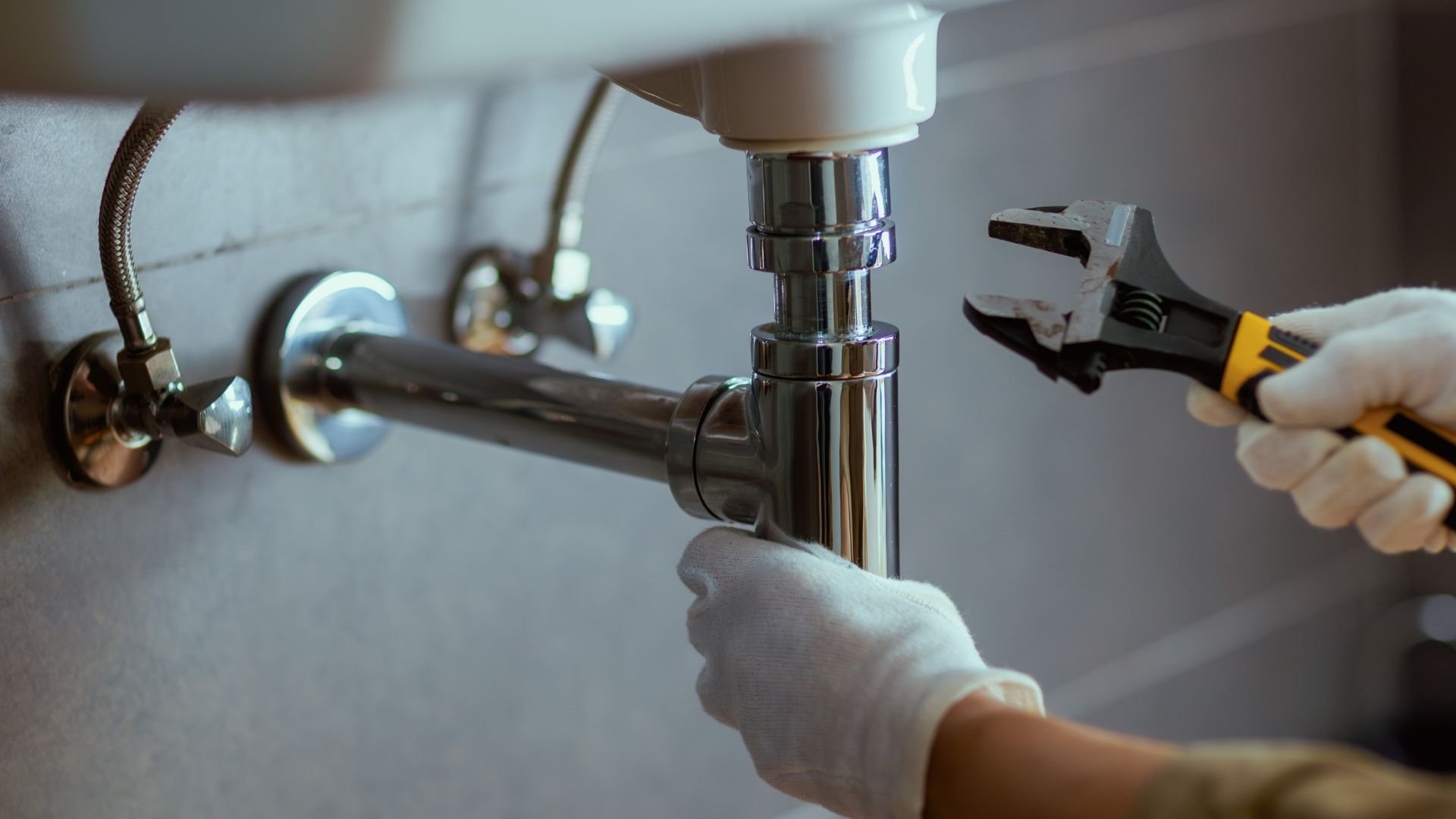 Plumber fixing sink pipe with wrench and gloved hands