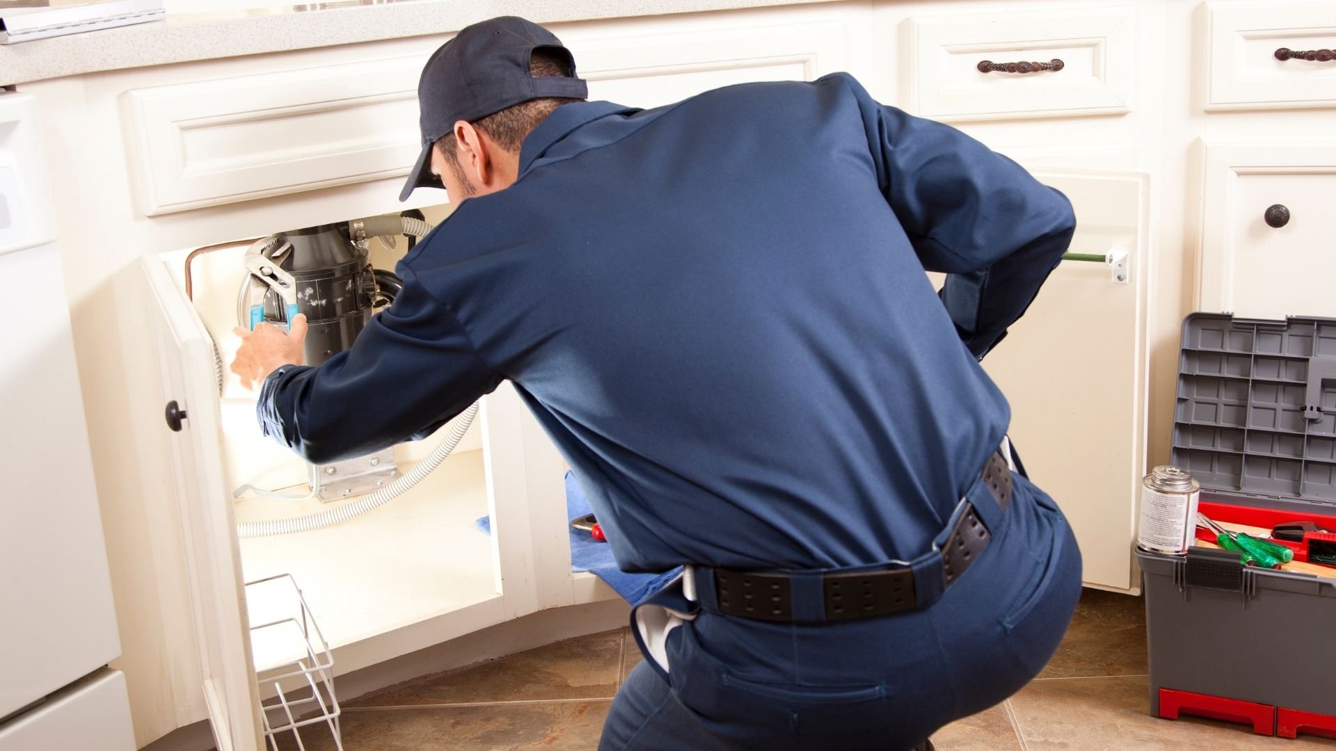 Technician in blue uniform repairing kitchen plumbing under sink
