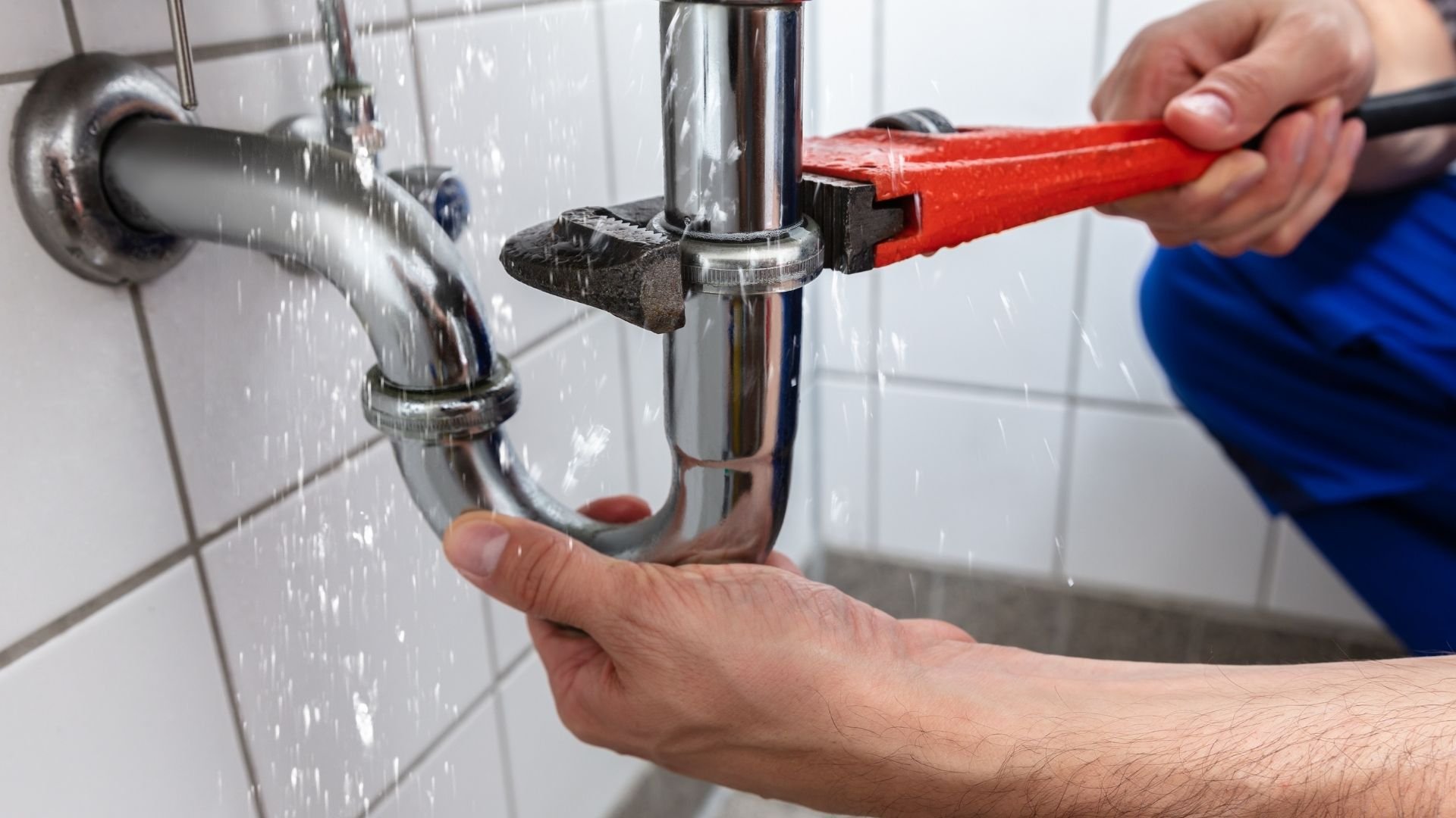 Plumber fixing leaking sink pipe with red wrench in tiled bathroom