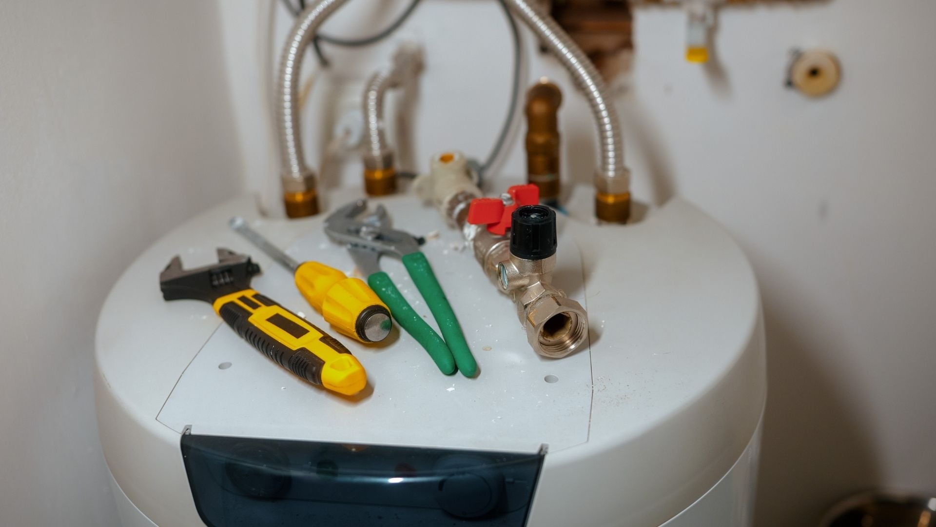 Tools and plumbing valves on top of a white water heater