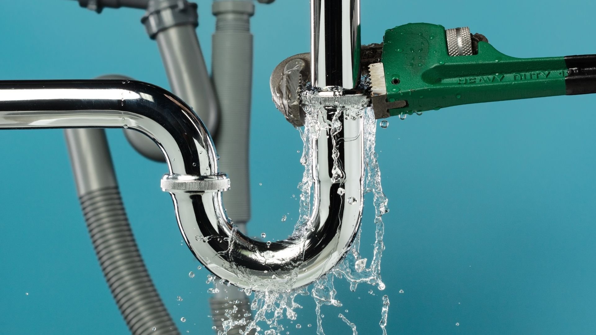 Water flowing through a metal P-trap pipe with a green wrench