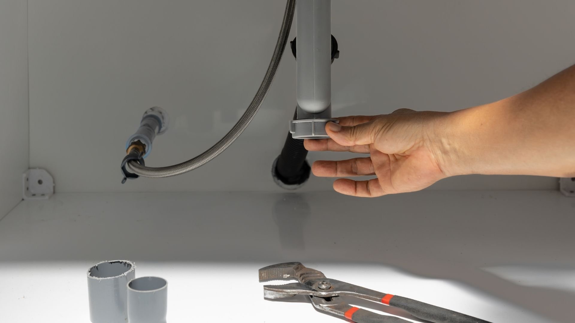 Plumbing repair with hand adjusting pipe fitting and pliers nearby