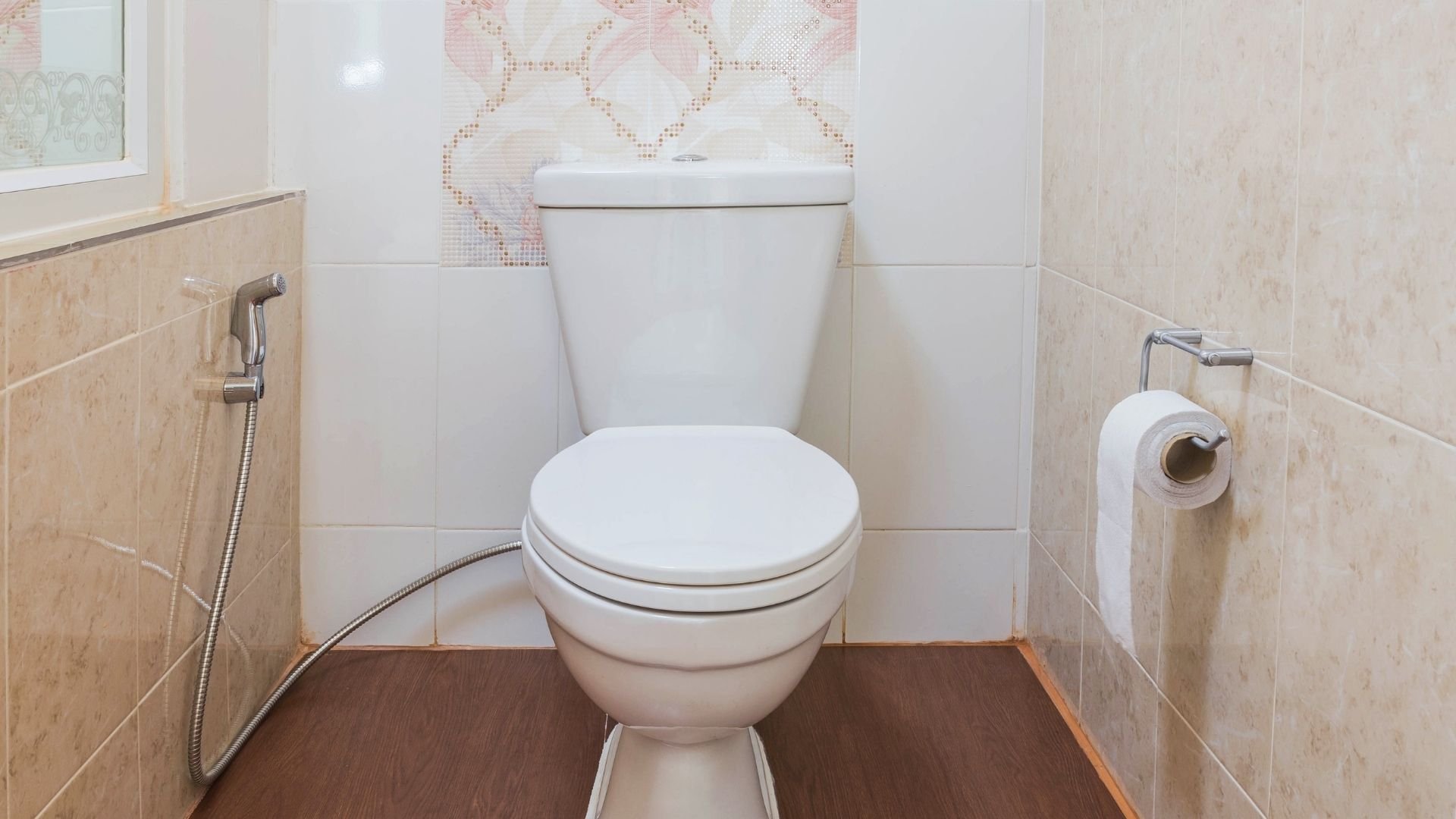 Clean white toilet with beige tiles and decorative mosaic wall accent