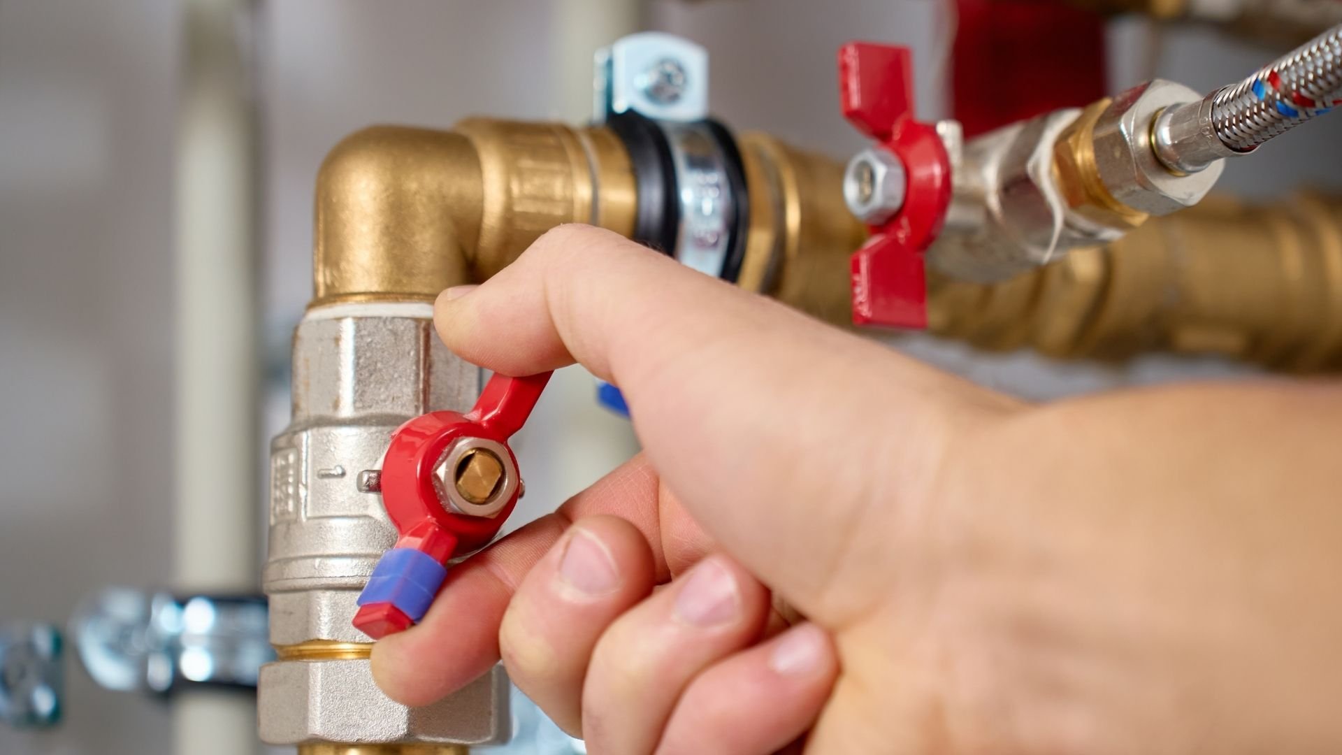 Hand adjusting red valve on brass plumbing pipes and connections
