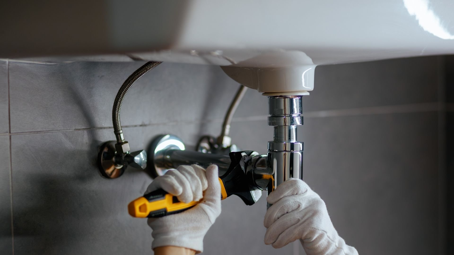 Plumber using wrench to repair sink pipes under bathroom basin