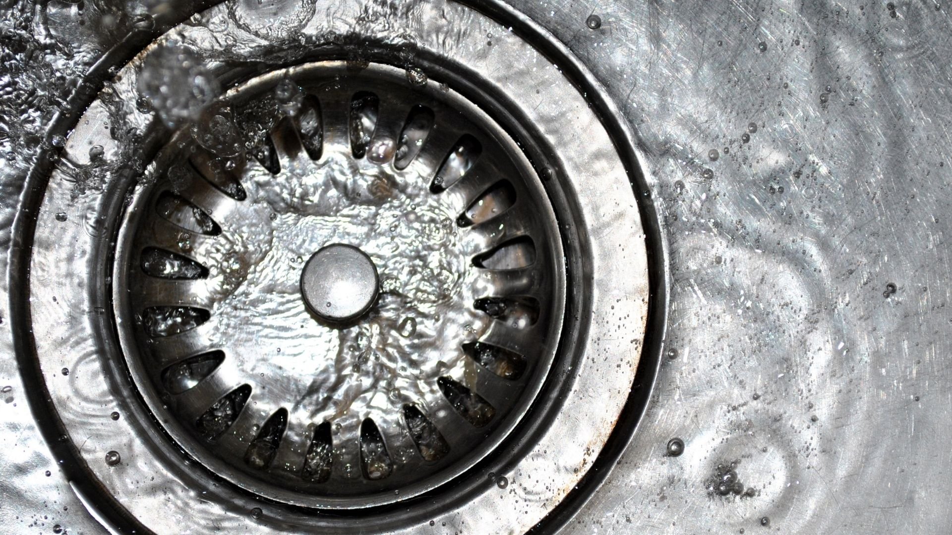 Close-up of a wet kitchen sink drain with water and metallic texture