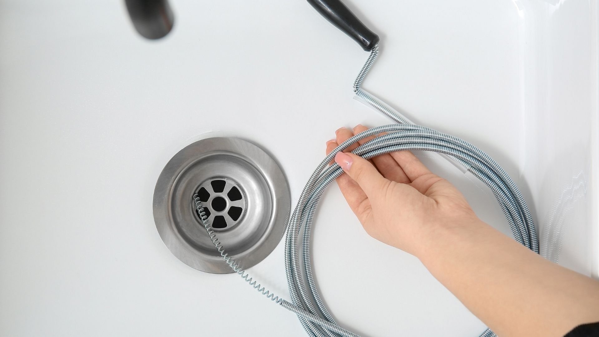 Drain snake being used to unclog a sink drain